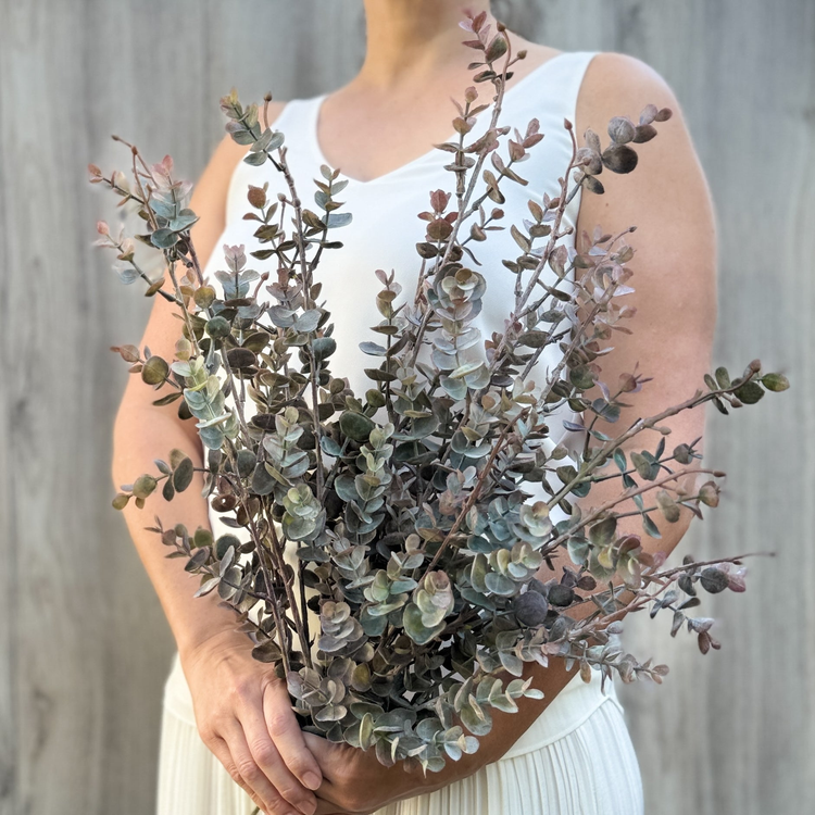 woman holding a bouquet of realistic artificial leaves.  the stems have many fake leaves and are a subdued green with copper tones.