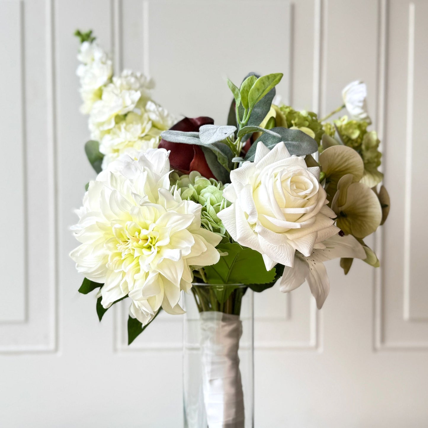 an artificial flower bridal bouquet featuring pale green artificial hydrangeas, white artificial dahlias, white artificial peonies, white artificial tea roses, white artificial Austin roses, and deep wine artificial calla lilies accented with soft lamb’s ear greenery — from My Faux Florist Canada.