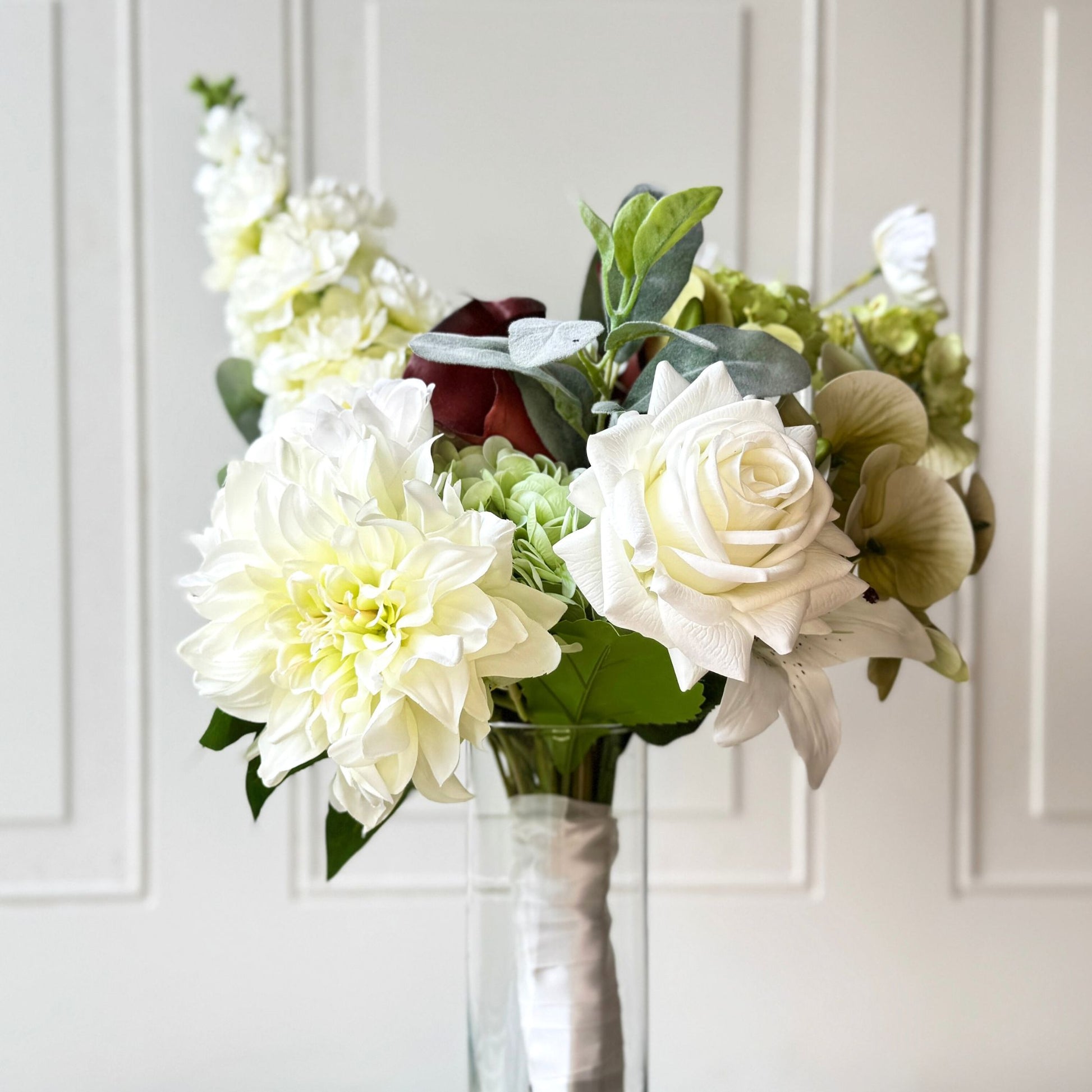 an artificial flower bridal bouquet featuring pale green artificial hydrangeas, white artificial dahlias, white artificial peonies, white artificial tea roses, white artificial Austin roses, and deep wine artificial calla lilies accented with soft lamb’s ear greenery — from My Faux Florist Canada.