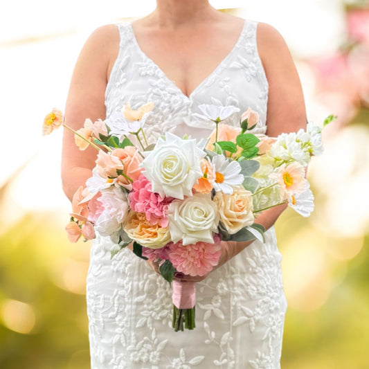 Bride holding a realistic artificial flower bridal bouquet featuring white artificial roses, blush artificial peonies, apricot artificial tulips, cream artificial tea roses, pink artificial hydrangeas, and white artificial cosmos — Real Touch flowers from My Faux Florist Canada.
