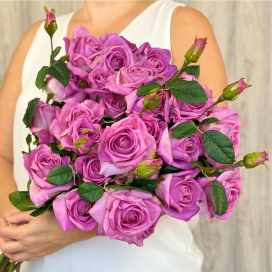 A premium mauve artificial rose stem held by a person, featuring two full 'tea rose' blooms and a delicate Real Touch rosebud with deep pink hues and subtle purple undertones by My Faux Florist.