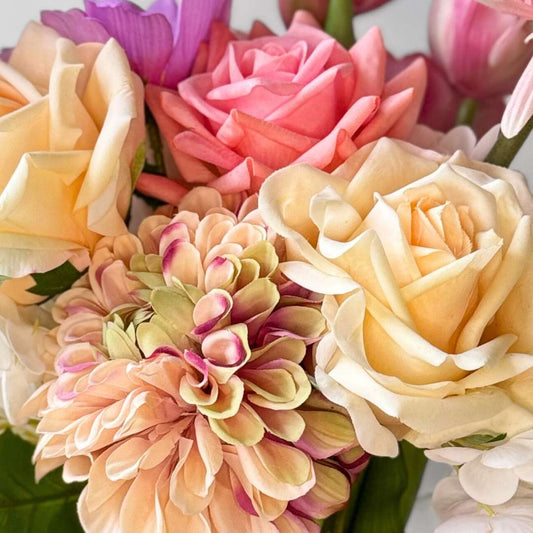 Close up of a realistic artificial flower bouquet featuring pink artificial tulips, champagne artificial tea roses, blush artificial peonies, white artificial hydrangeas, pink artificial dahlias, and lavender artificial cosmos tied with a satin ribbon — from My Faux Florist Canada.