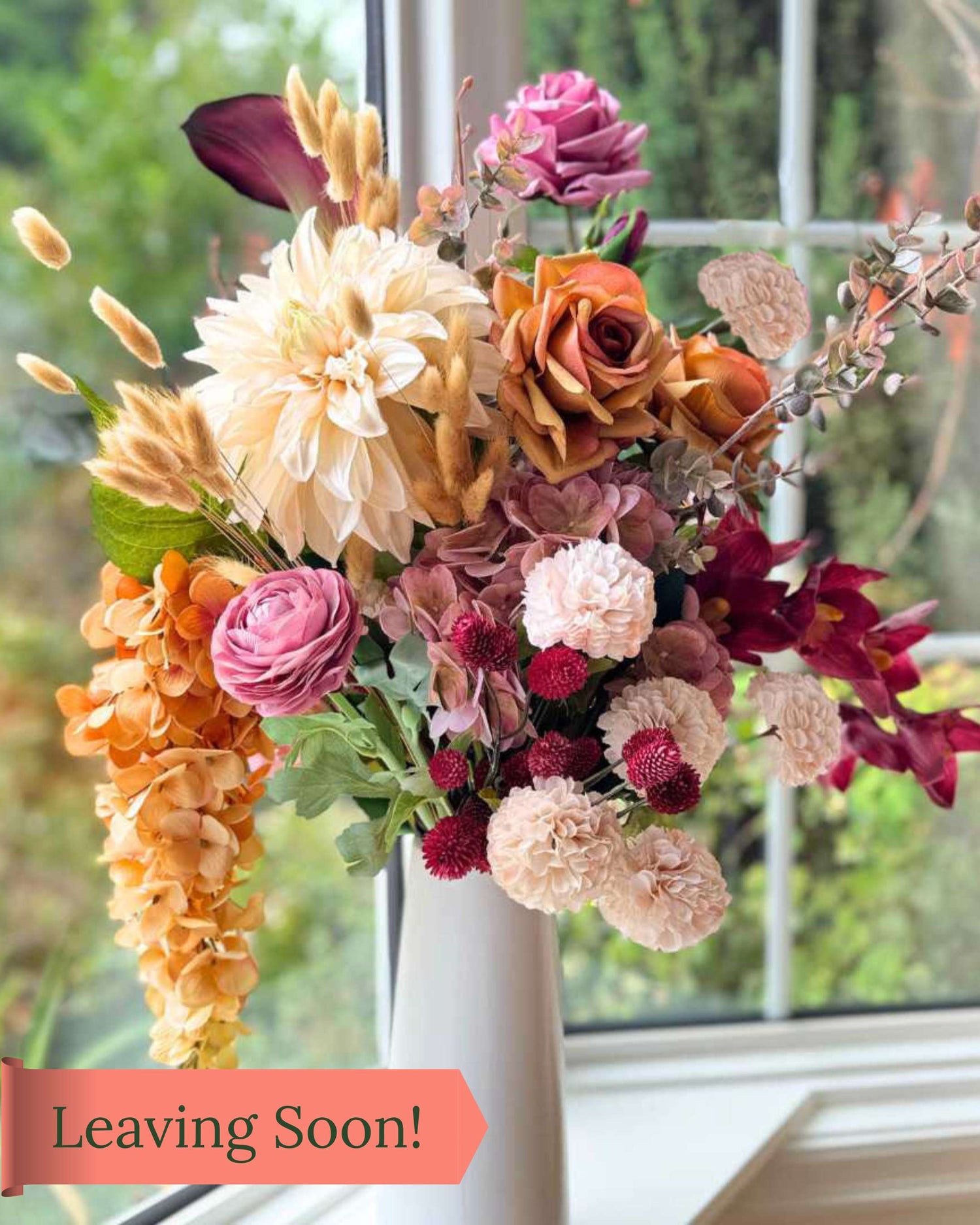Realistic artificial flower arrangement in a tall white vase featuring cream artificial dahlias, apricot artificial roses, mauve artificial roses, pink artificial ranunculus, blush artificial hydrangeas, burgundy artificial orchids, red artificial billy balls, and golden artificial hanging orchids — from My Faux Florist Canada.