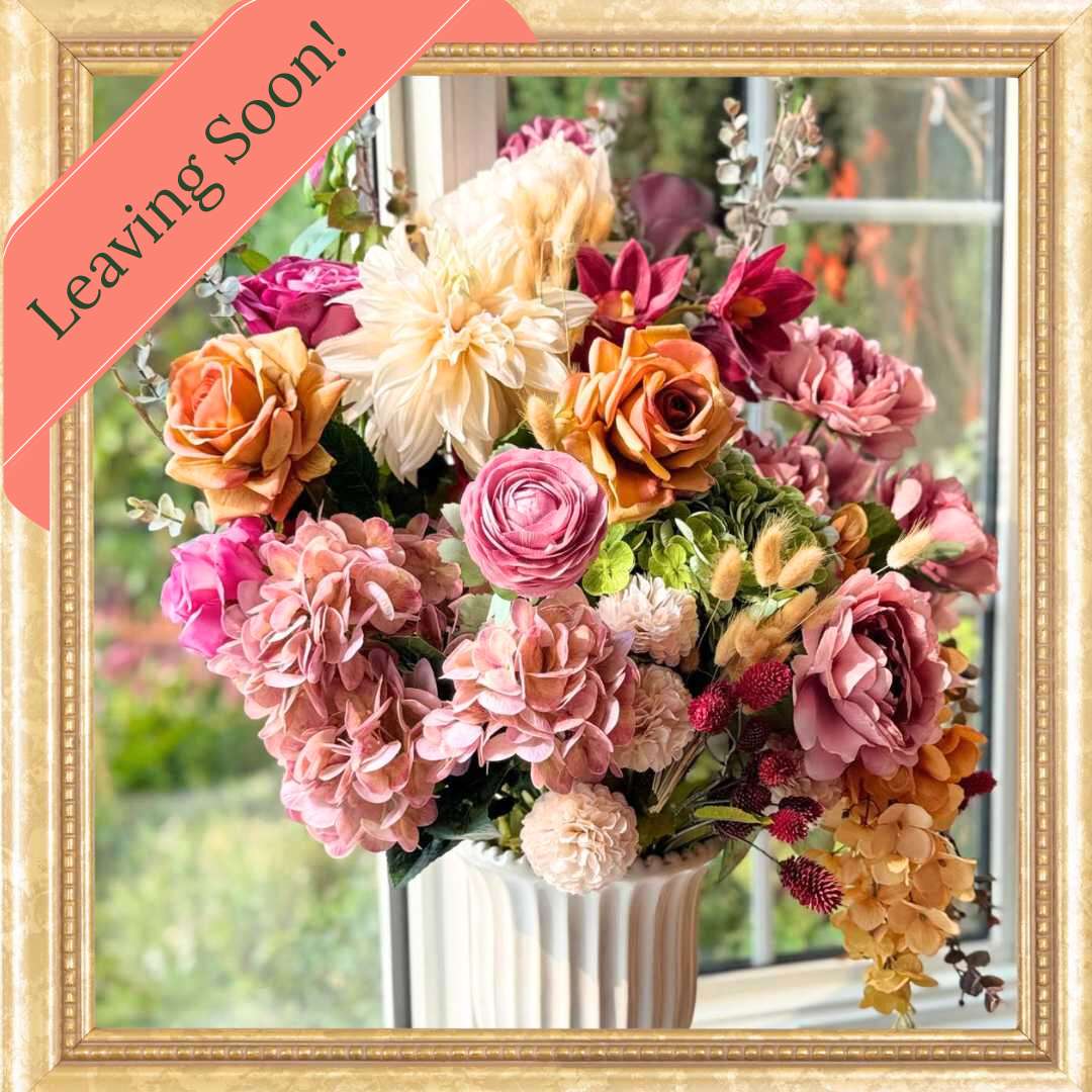 Realistic artificial flower arrangement in a white vase featuring cream artificial dahlias, apricot artificial roses, mauve artificial roses, pink artificial hydrangeas, blush artificial peonies, green artificial hydrangeas, burgundy artificial ranunculus, and golden artificial orchids — from My Faux Florist Canada.