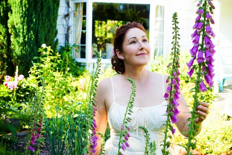 Artificial Flowers Canada. Woman in a sunlit garden surrounded by blooming foxglove flowers. About Us photo for My Faux Florist.