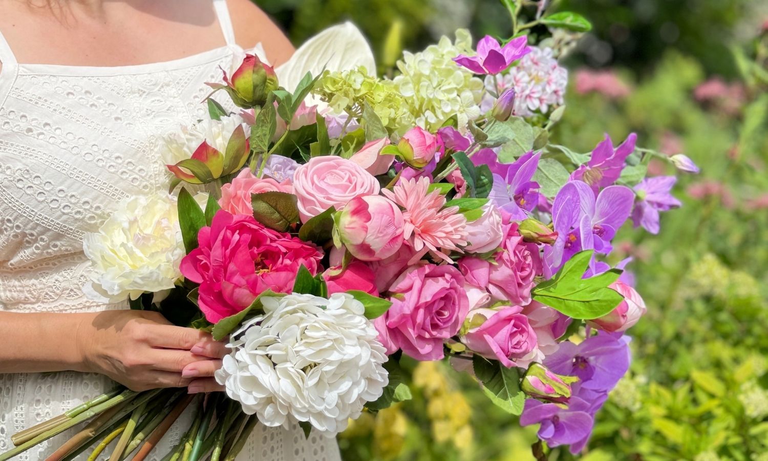 Bouquet of colorful realistic artificial flowers held by a person in a white dress against a blurred green background for My Faux Florist Canada