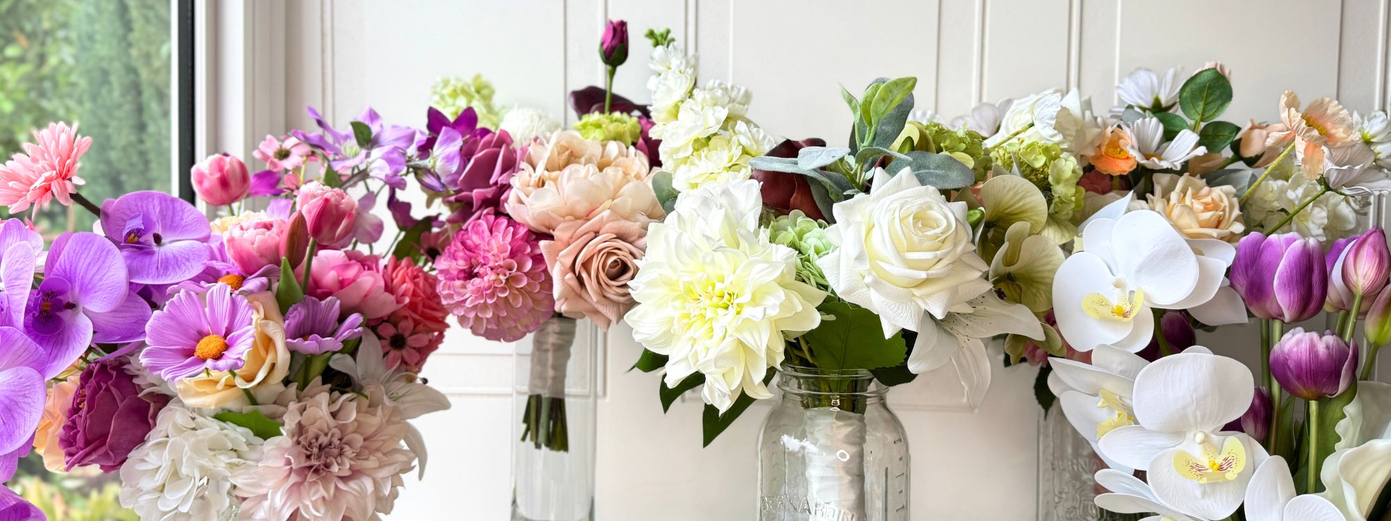Collection of realistic artificial flower bridal bouquets displayed in glass vases featuring purple artificial orchids, pink artificial dahlias, blush artificial peonies, champagne artificial roses, white artificial dahlias, pale green artificial hydrangeas, white artificial orchids, and lavender artificial tulips — from My Faux Florist Canada.
