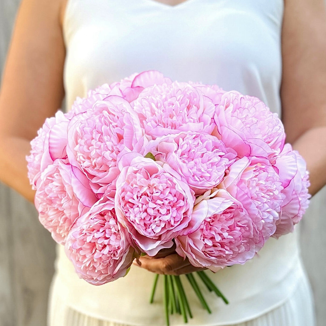 Person holding a bouquet of pink faux peonies in front of a neutral background, by My Faux Florist artificial flowers Canada.