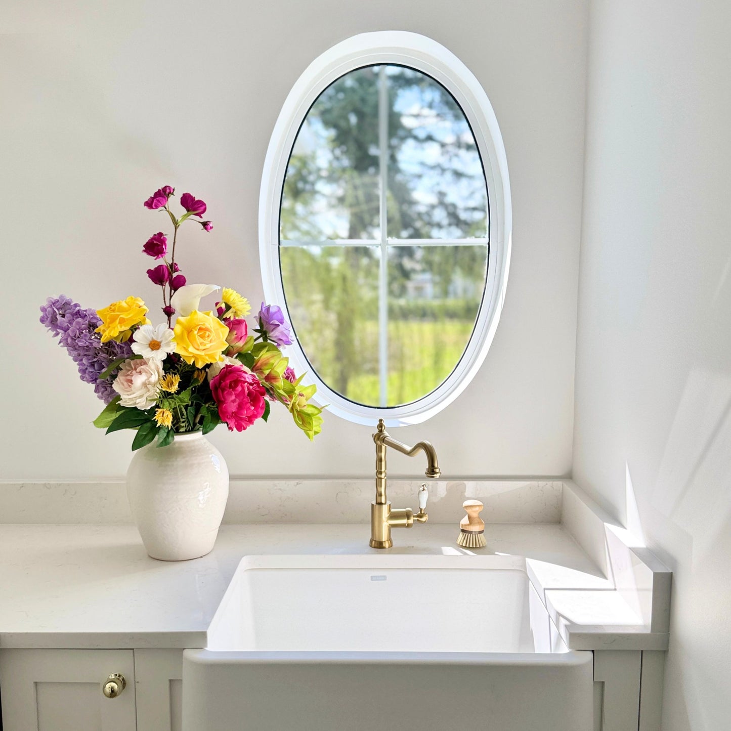 Vase of colourful and realistic artificial flowers next to a white sink and an oval window. Faux peonies, faux roses, faux hydrangea, and faux orchids in an artificial flower bouquet for My Faux Florist Canada.