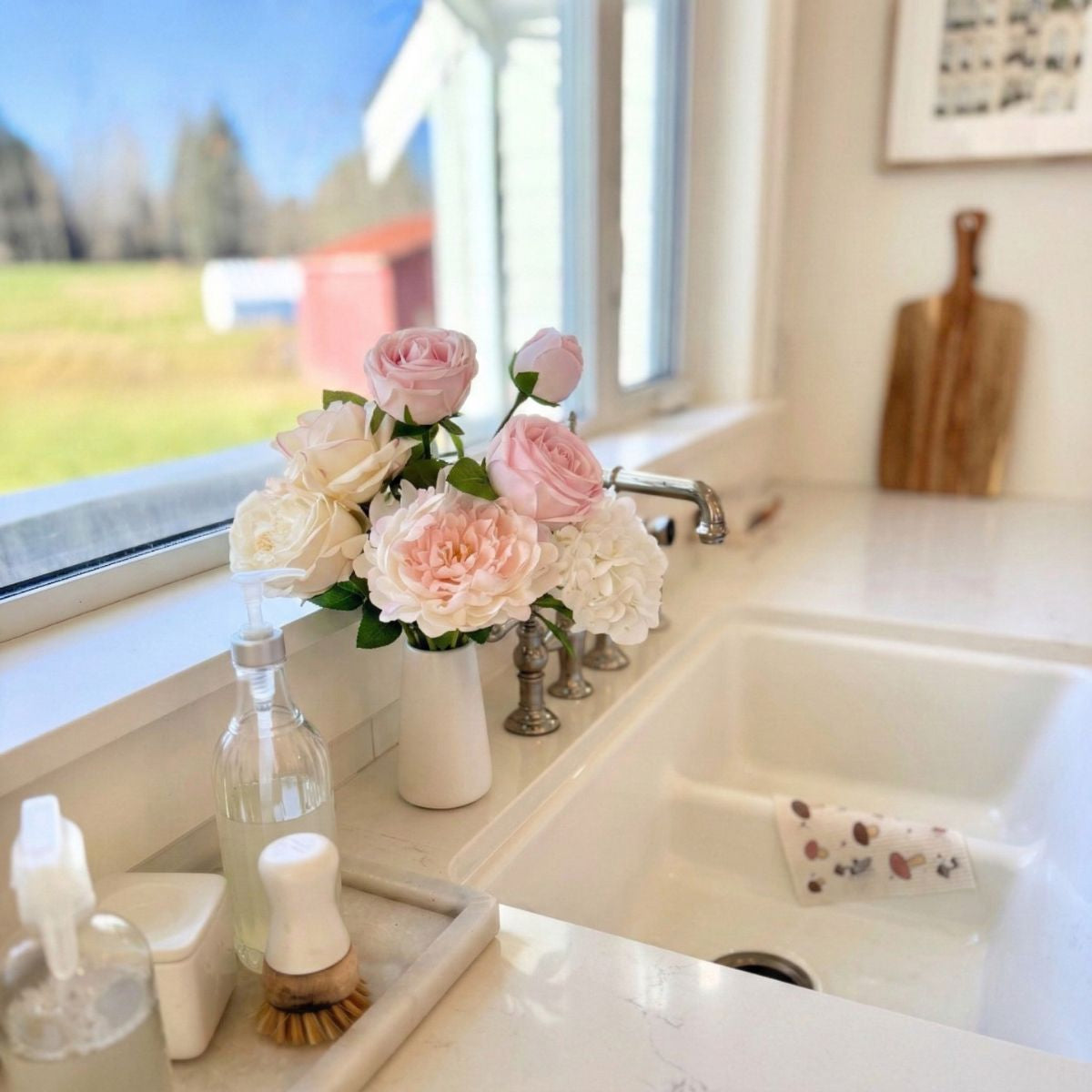 Kitchen sink area with realistic artificial flowers and cleaning supplies near a window, for My Faux Florist Canada