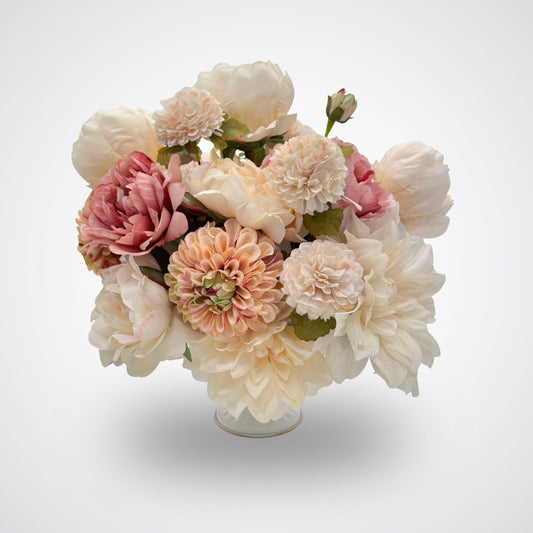 A bouquet of artificial flowers in a clear glass vase, featuring cream, blush pink, and peach blooms with green foliage, set against a light gray background. A realistic artificial flower arrangement for Fall. Artificial flowers from My Faux Florist Canada.