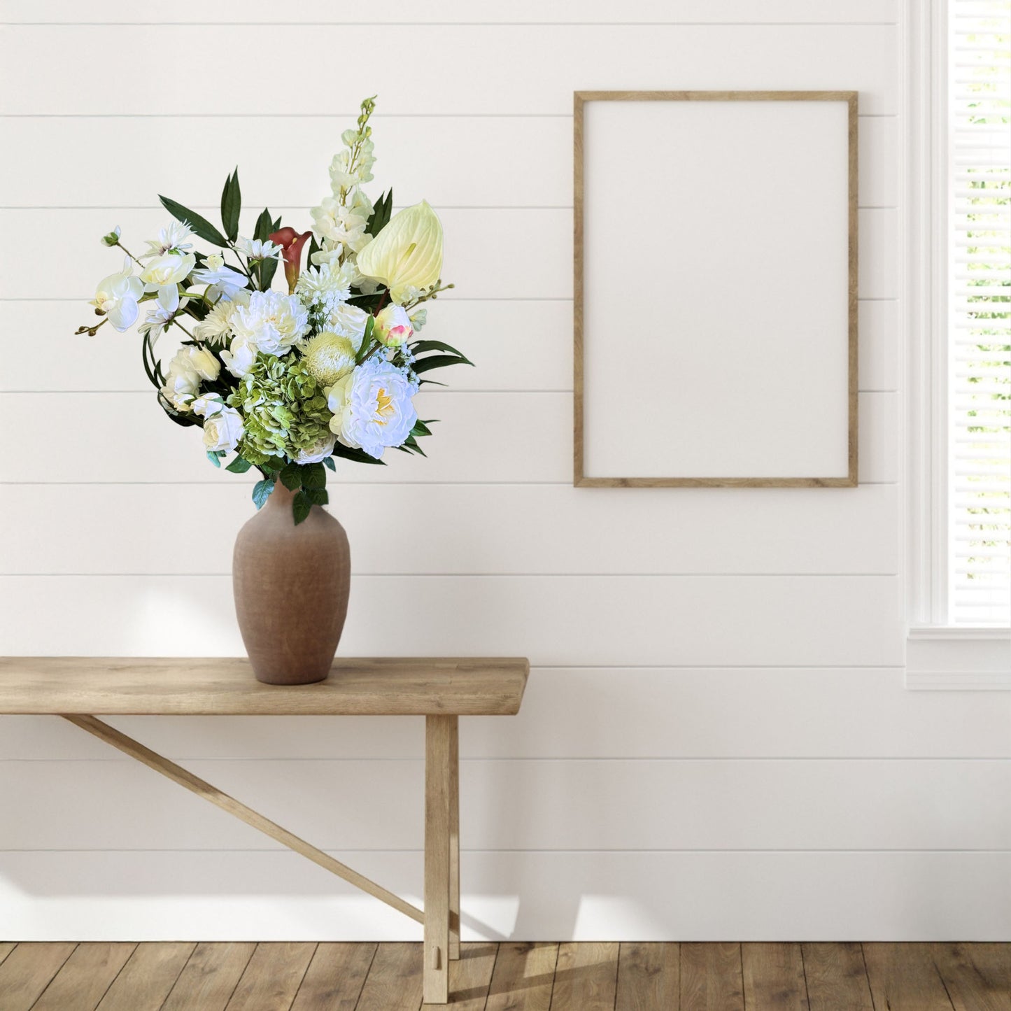 Vase with neutral coloured artificial flowers on a wooden table against a white wall with a framed picture, by My Faux Florist artificial flowers Canada.