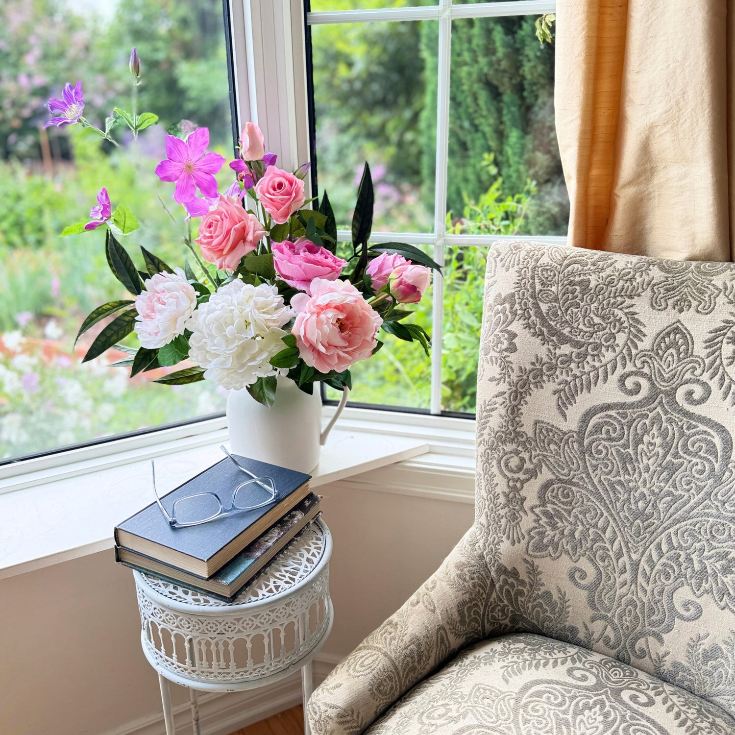 ealistic artificial flower arrangement in a white pitcher featuring pink artificial roses, blush artificial peonies, white artificial dahlias, and purple artificial cosmos, styled on a windowsill beside books and a patterned armchair — from My Faux Florist Canada.