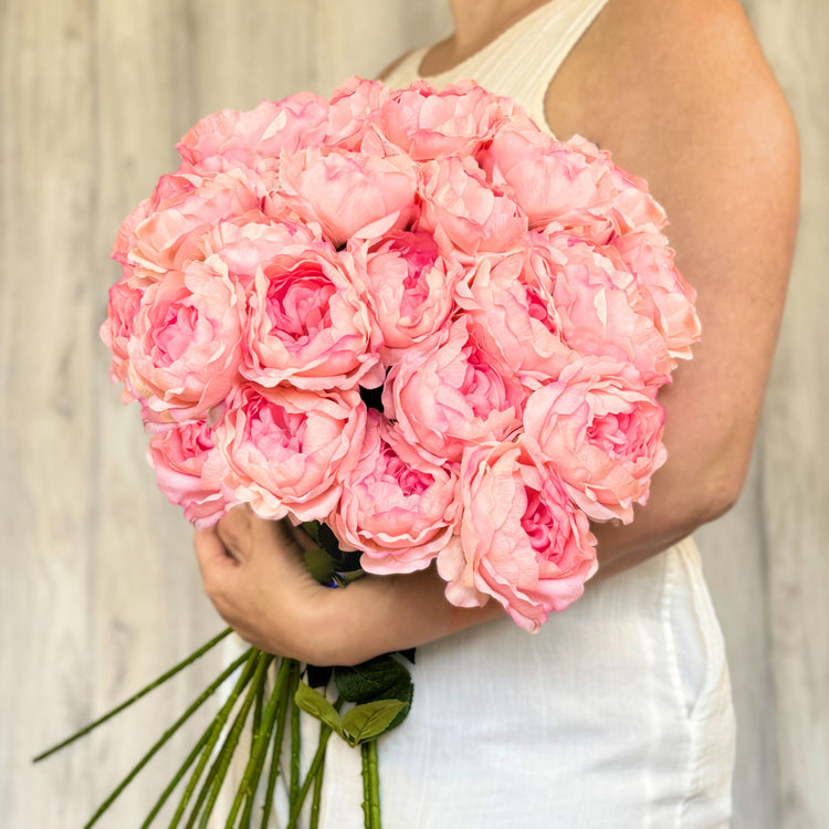 Bundle of pink faux peonies held in front of a neutral wood background.