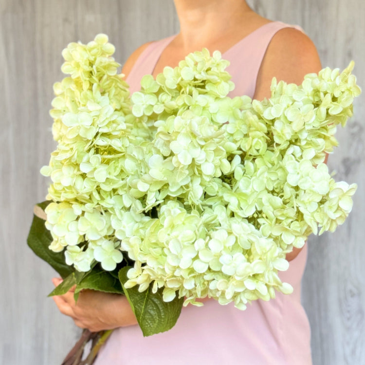Woman in pink holding bouquet of pale green artificial hydrangeas