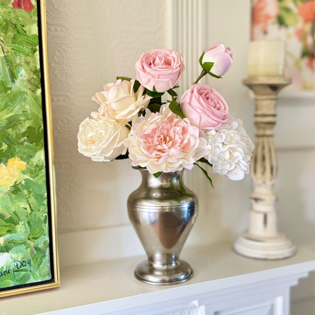 Artificial flower bouquet in a white vase featuring faux roses, faux peonies, artificial gladioli and greenery on a windowsill