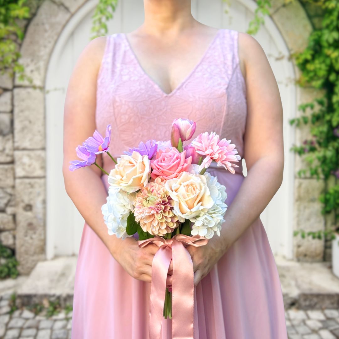 Bridesmaid holding a realistic artificial flower bouquet featuring pink artificial tulips, champagne artificial tea roses, blush artificial peonies, white artificial hydrangeas, pink artificial dahlias, and lavender artificial cosmos tied with a satin ribbon — from My Faux Florist Canada.
