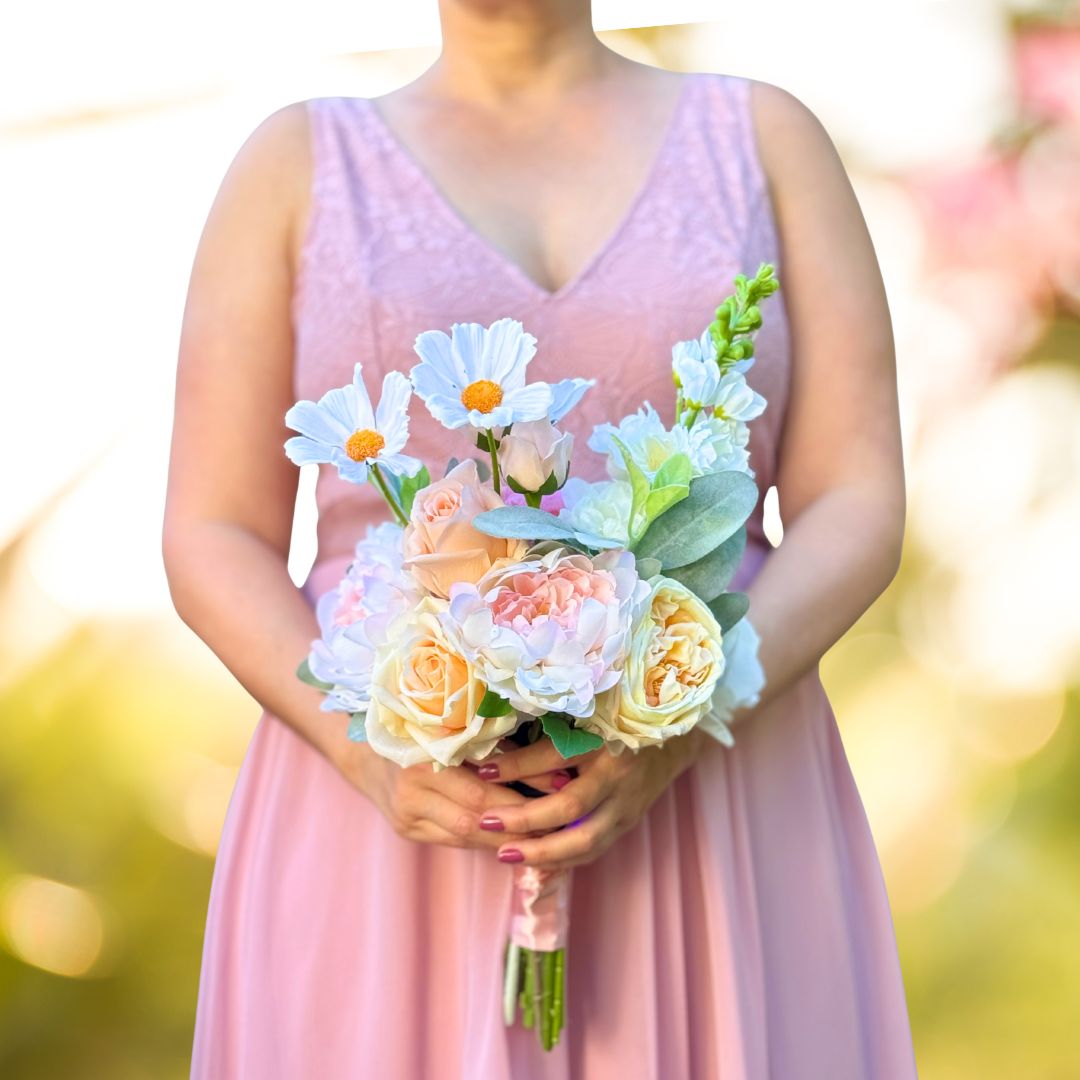 Bridesmaid holding a realistic artificial flower bouquet featuring white artificial cosmos, blush artificial peonies, apricot artificial tulips, cream artificial tea roses, pink artificial hydrangeas, and pale green artificial stock with lamb’s ear greenery — from My Faux Florist Canada.