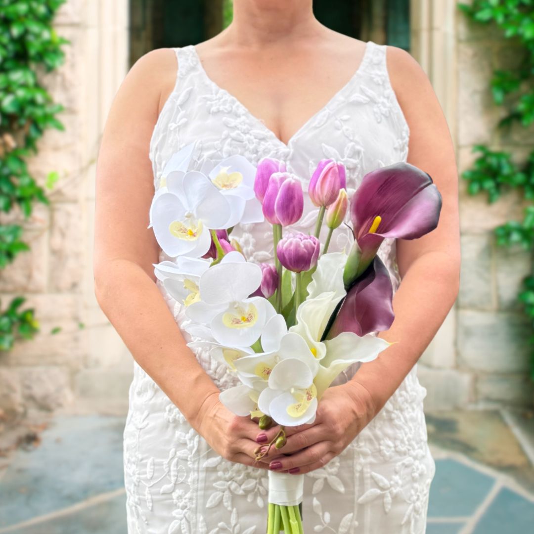 Bride holding an artificial flower bridal bouquet featuring white artificial orchids, deep wine artificial calla lilies, white artificial calla lilies, and lavender artificial tulips — from My Faux Florist Canada.