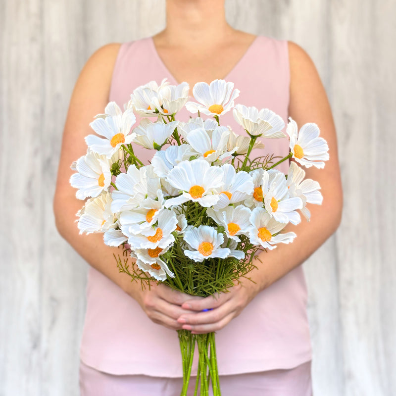 A person holding a bouquet of artificial white cosmos flowers.