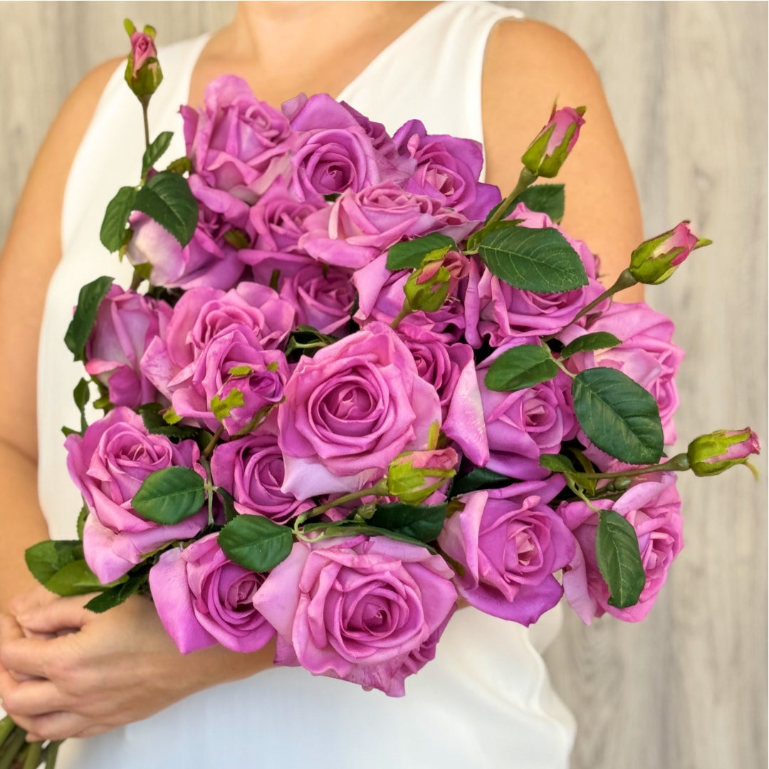 A premium mauve artificial rose stem held by a person, featuring two full 'tea rose' blooms and a delicate Real Touch rosebud with deep pink hues and subtle purple undertones by My Faux Florist.
