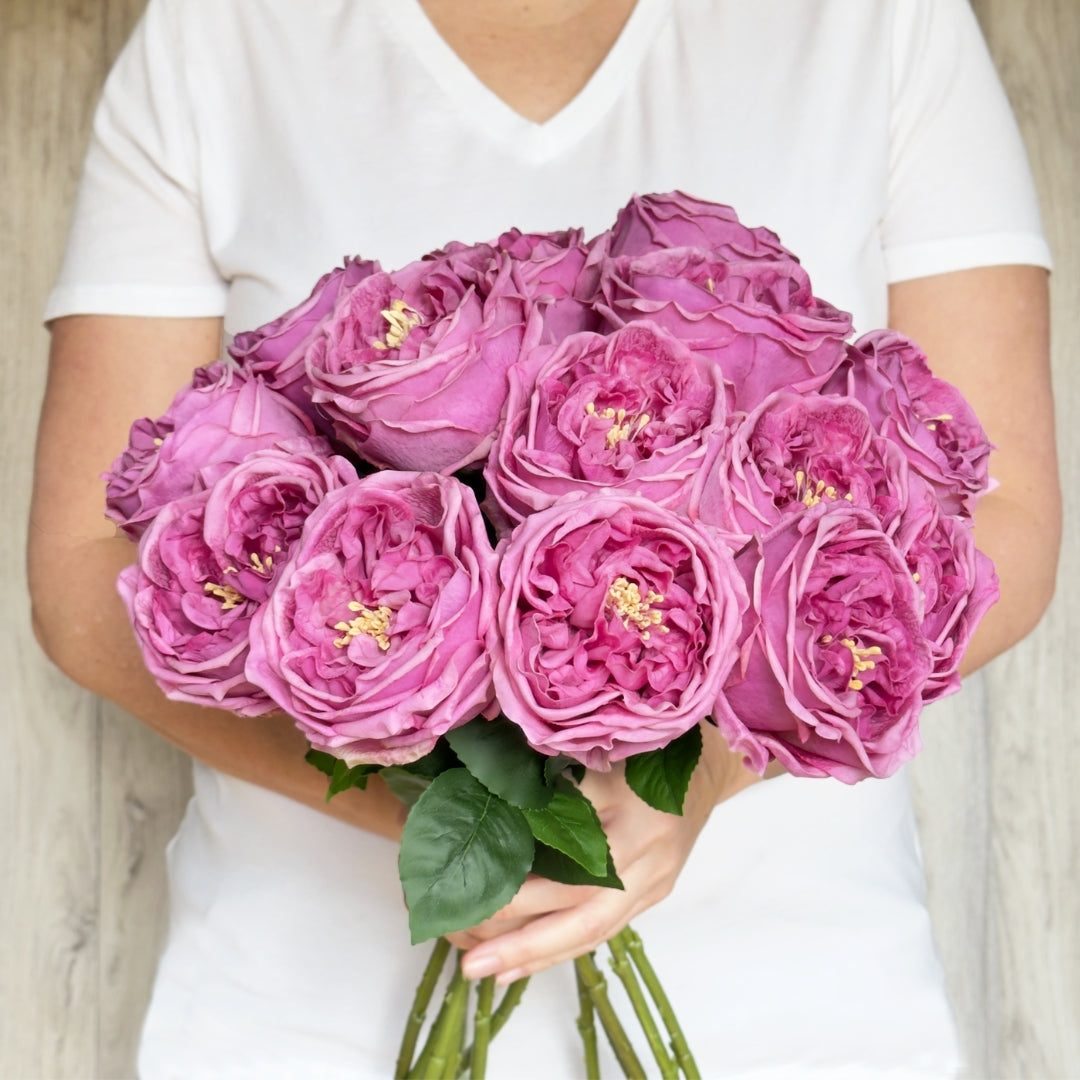 A person holding a bouquet of dark pink Austin rose style artificial roses with green leaves and Real Touch petals, by My Faux Florist Canada