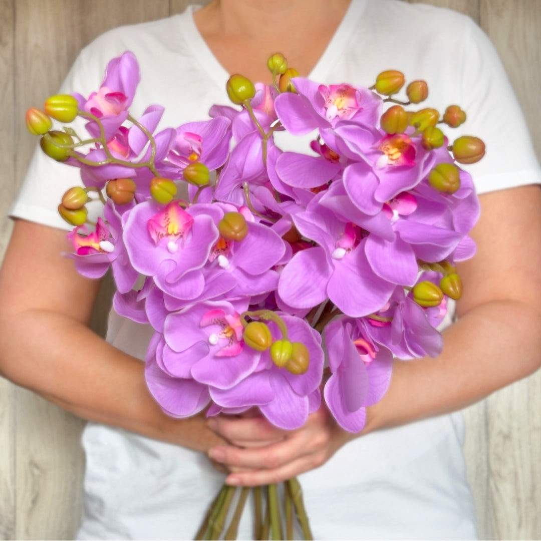 A person holding a bouquet of bright pink fuchsia artificial orchid flowers with Real Touch petals by My Faux Florist Canada.