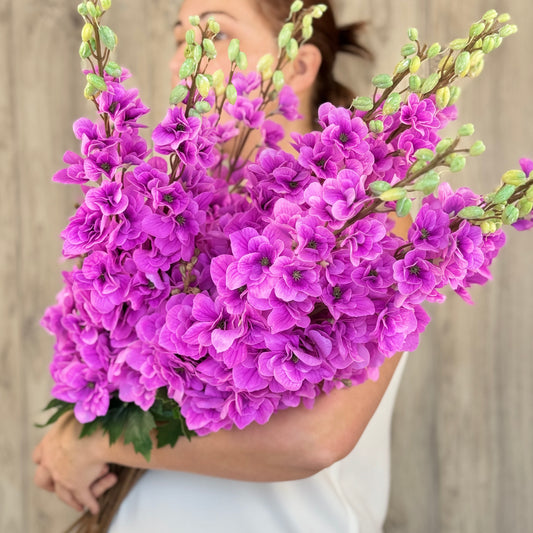 A person holding a bouquet of fuchsia artificial delphinium flowers with lifelike Real Touch details, by My Faux Florist Canada