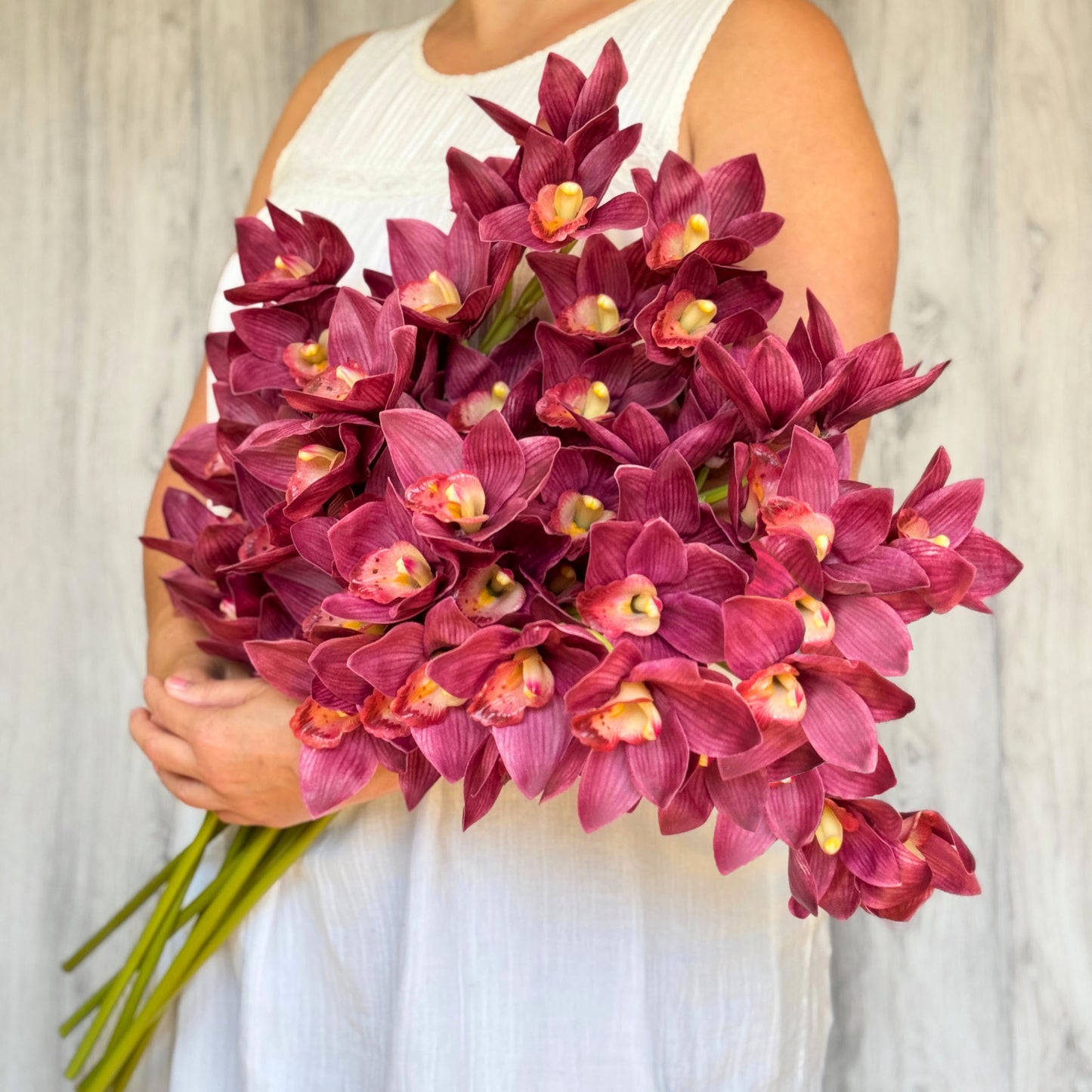 A person holding a bouquet of deep wine coloured artificial orchid flowers from My Faux Florist Canada