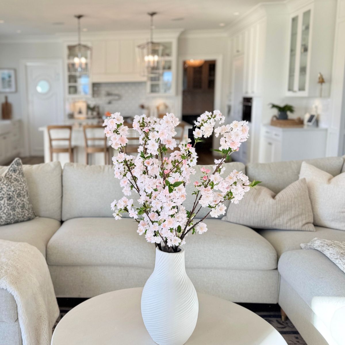 White vase with pink cherry blossom artificial flowers on a coffee table in a living room, for My Faux Florist Canada.