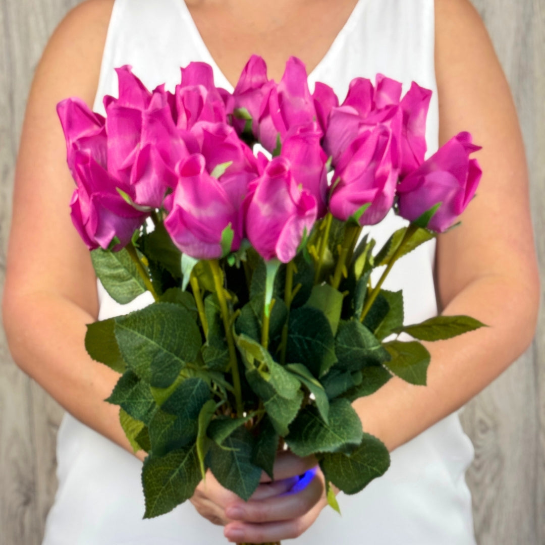 A person holding a bouquet of fuchsia artificial pink rosebuds with green leaves from My Faux Florist Canada