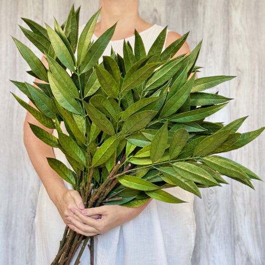 Woman holding tall artificial willow greenery bundle in front of her, by Faux Florist Canada