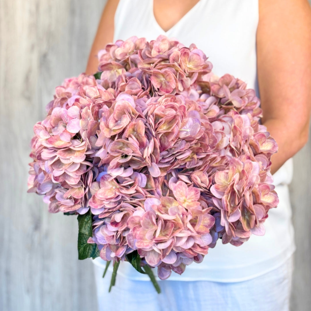 A person holding a medium pink artificial hydrangea bush with subtle purple undertones and realistic Real Touch veining. Realistic fake flowers by  My Faux Florist Canada