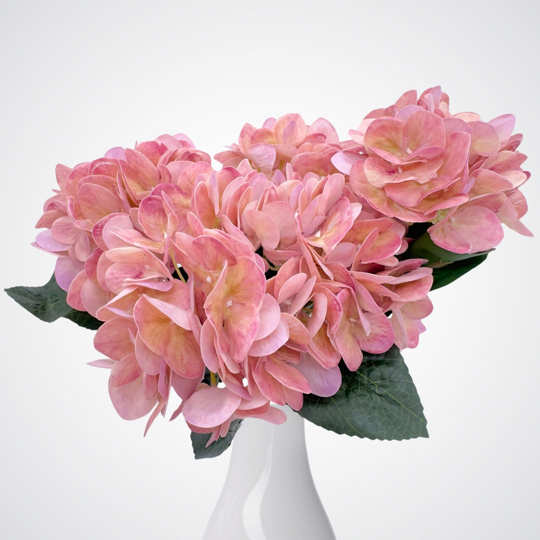 White vase containing medium pink artificial hydrangea bush with subtle purple undertones and realistic Real Touch veining. Realistic fake flowers by  My Faux Florist Canada