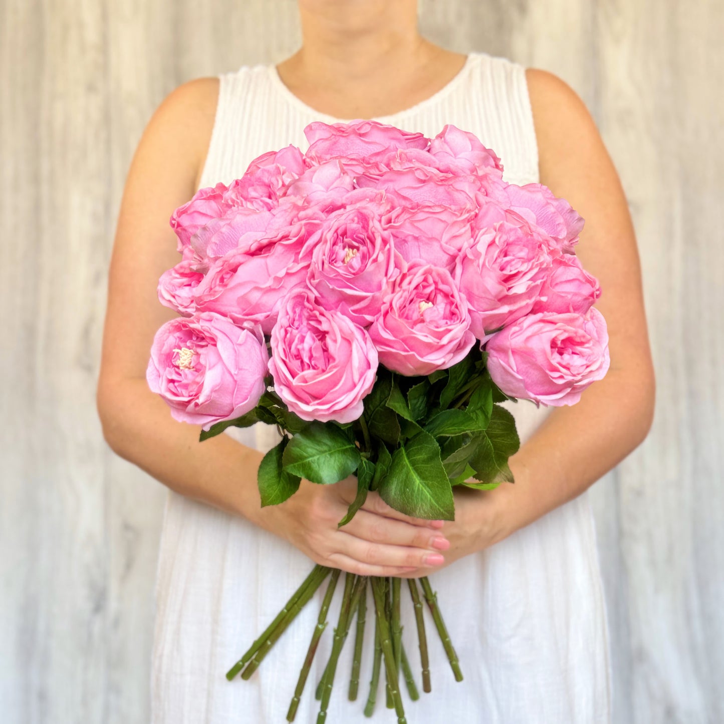 A person holding a bouquet of Austin style artificial roses in a deep pink colour with realistic Real Touch petals, from My Faux Florist artificial flowers Canada.