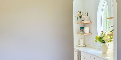 bright white kitchen counter displays an oval window above a sink, next to a white vase of realistic artificial flowers for My Faux Florist Canada.