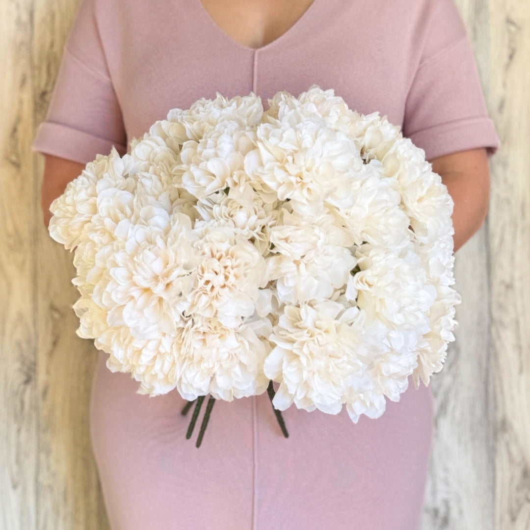 A person holding a bouquet of ivory artificial dahlia bushes with full, round-shaped petals by My Faux Florist Canada