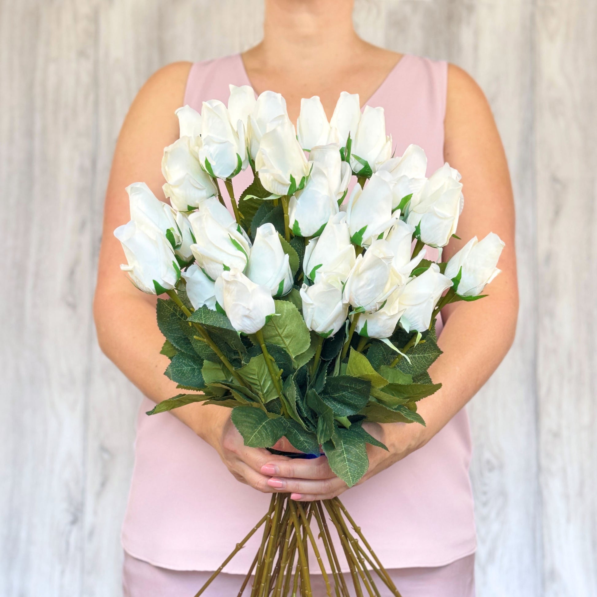 A person holding a bunch of white artificial rose buds with green leaves.
