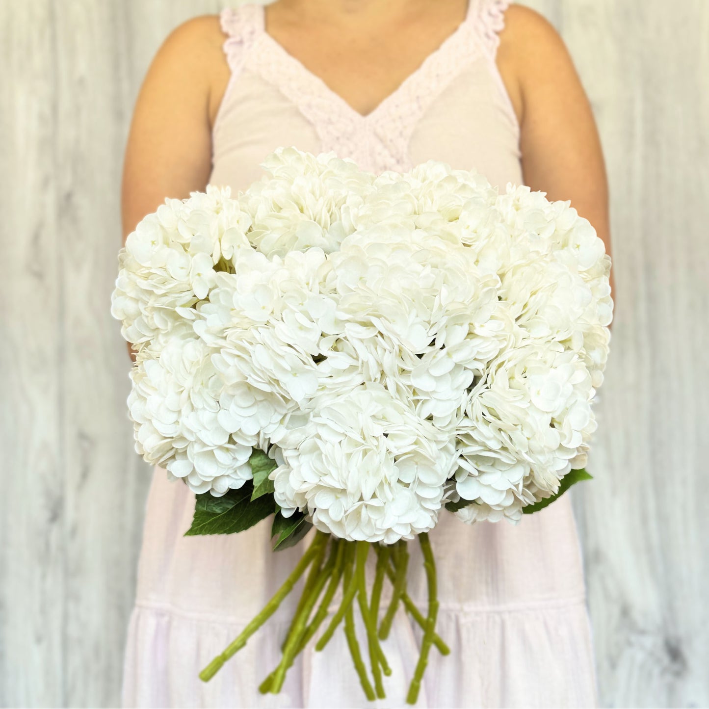 A person holding a large bouquet of white artificial hydrangea flowers.