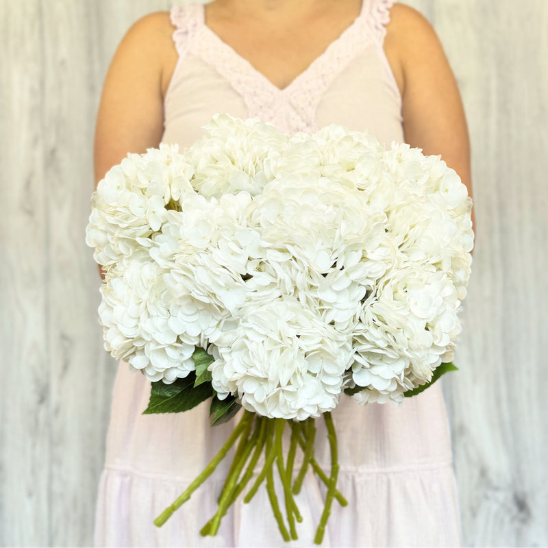 A person holding a large bouquet of white artificial hydrangea flowers.