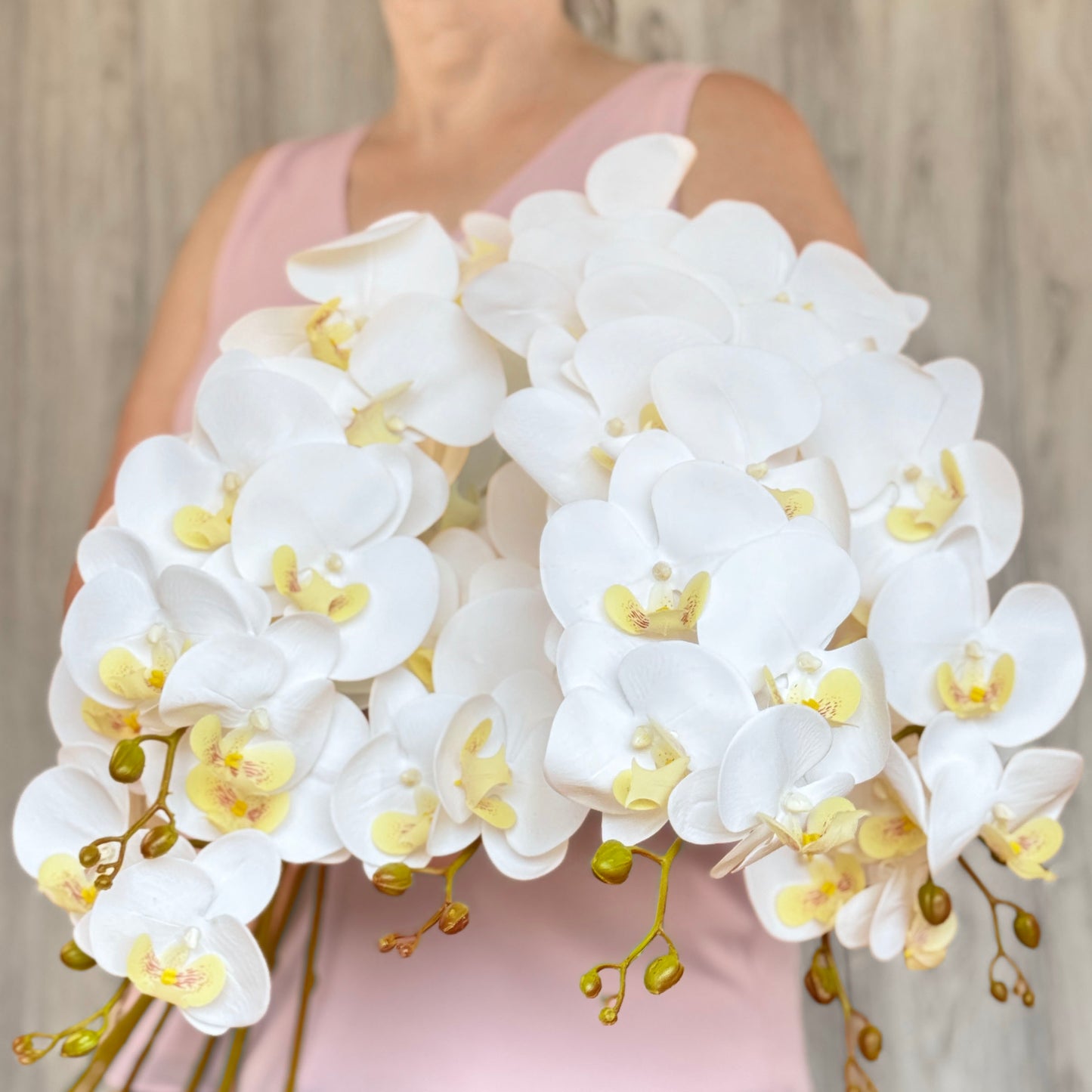 A person holding an mass of white  artificial orchid flowers from My Faux Florist Canada..