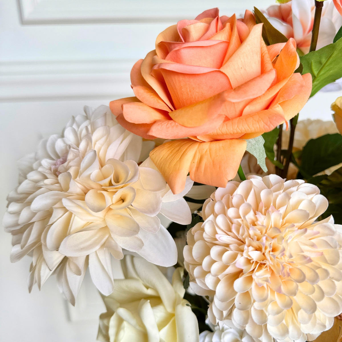A close-up of artificial flowers, featuring a prominent peach-orange Real Touch rose, a large cream Real Touch dahlia, and another cream faux rose in the background. For My Faux Florist Canada.