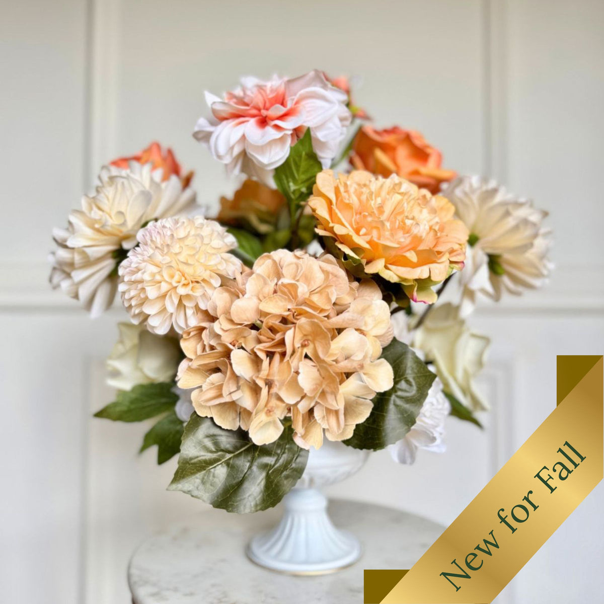 A bouquet of realistic artificial fall flowers in a white pedestal vase, featuring peach, orange, cream, and white blooms with green leaves, set against a white paneled wall with a gold 'New for Fall' banner overlay. For My Faux Florist Canada.
