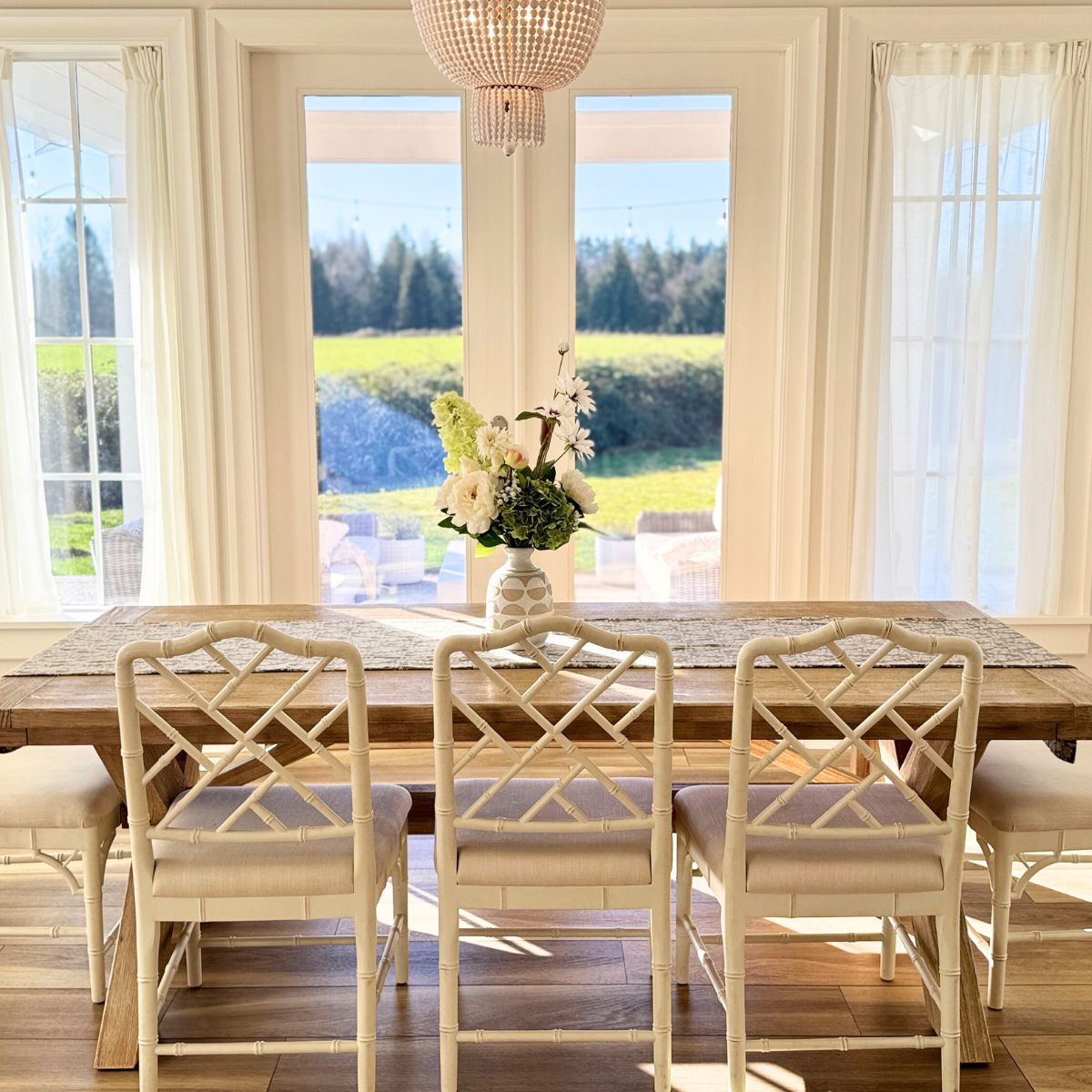 Dining room with wooden table and chairs, large windows, and outdoor view. Floral arrangement of artificial flowers in a vase on  table, for My Faux Florist Canada