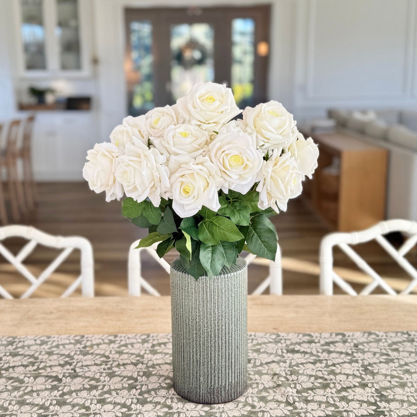 Bouquet of realistic white artificial roses in a textured vase on a table with a blurred indoor background - for My Faux Florist Canada.
