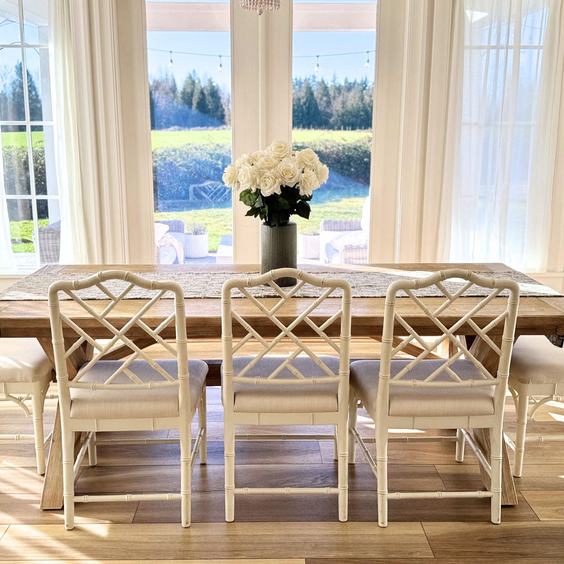 Dining room with wooden table and white chairs, large windows with curtains, and a vase of realistic artificial roses - for My Faux Florist Canada.