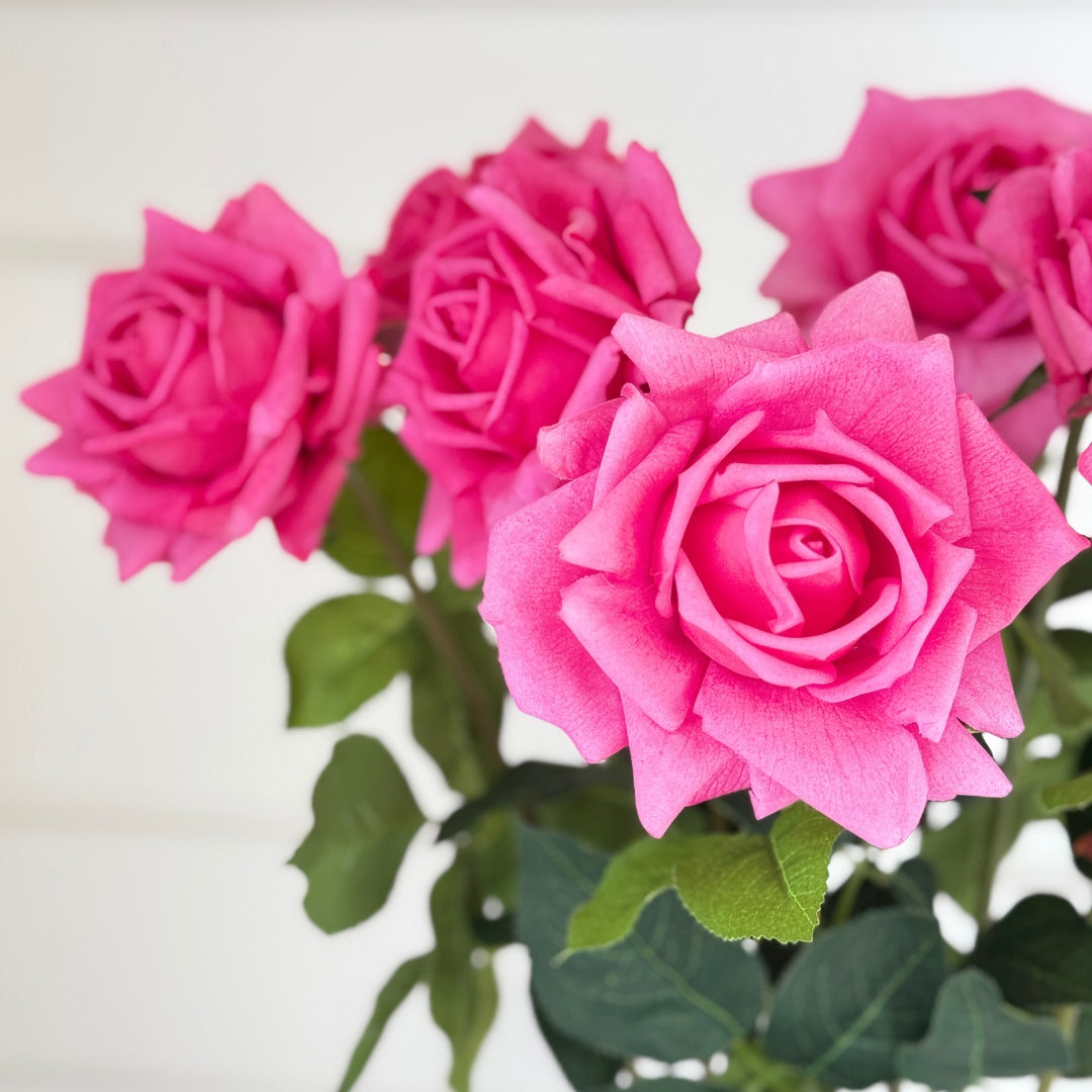 Artificial flowers in a vase on white background shows numerous realistic fuchsia pink artificial roses with realistic Real Touch bloom.