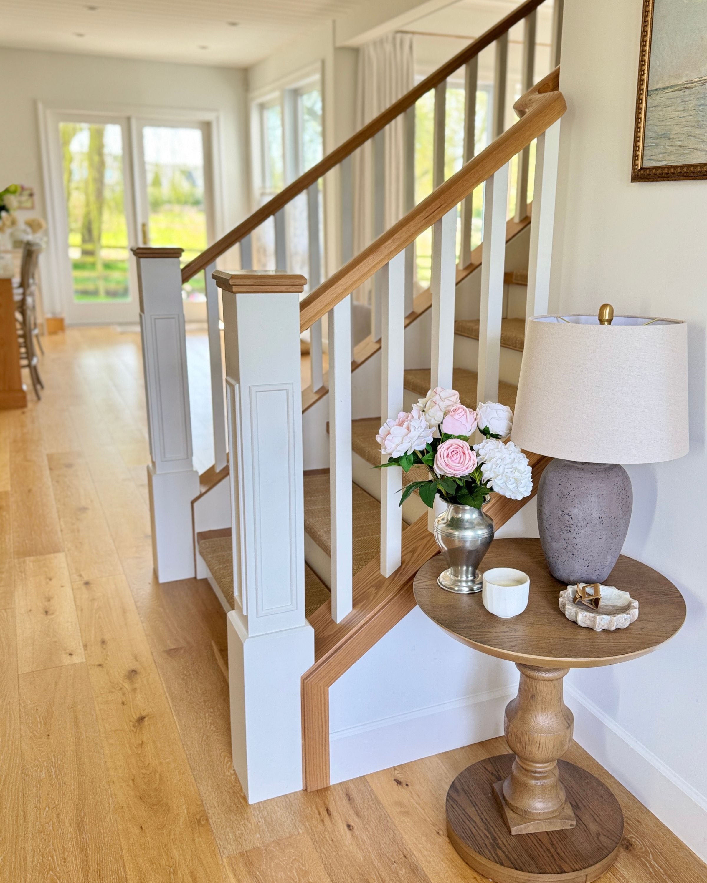 Staircase with wooden handrail and side table with lamp and a vase of realistic artificial flowers in a bright home interior. Faux peonies, faux roses, faux hydrangea,  in an artificial flower bouquet for My Faux Florist Canada.