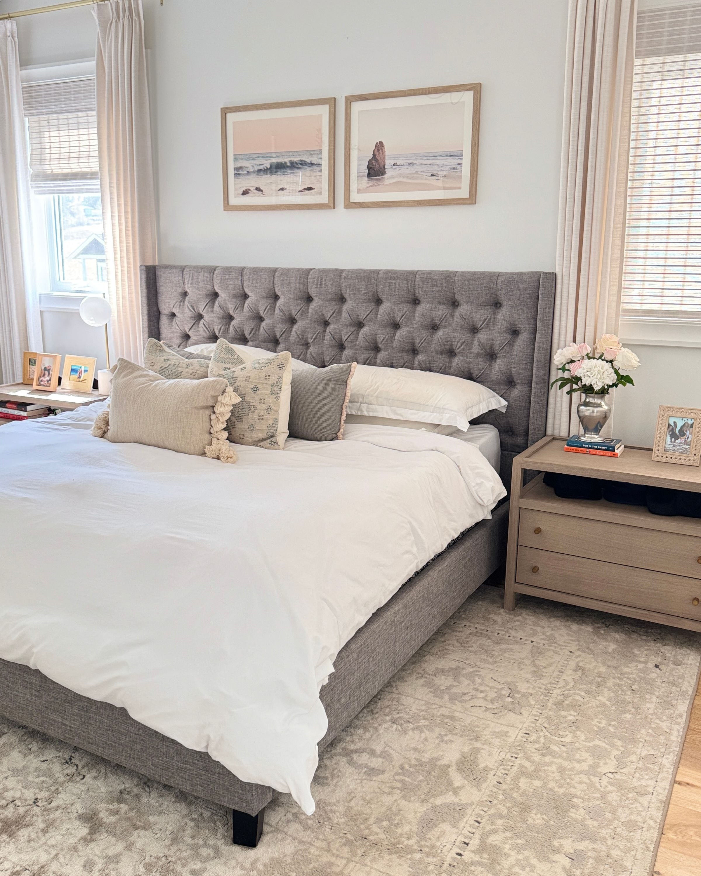 Neatly made bed with gray upholstered headboard in a bedroom setting, with a vase of realistic artificial flower on the bedside table.  Faux peonies, faux roses, faux hydrangea, in an artificial flower bouquet for My Faux Florist Canada.