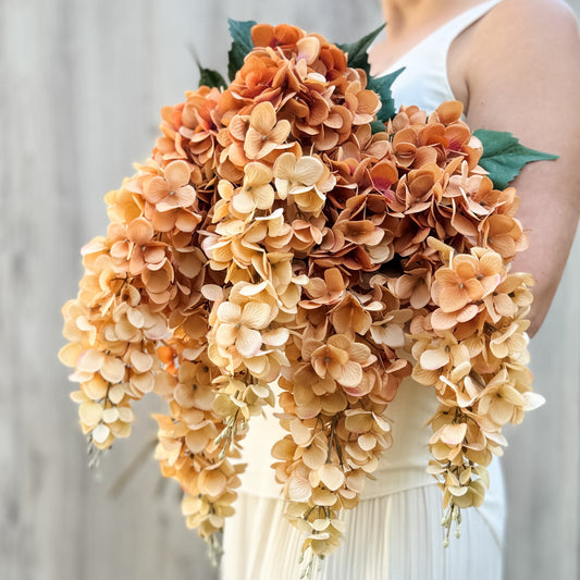 Person holding an armful of an artificial wisteria branches in ombre orange and bronze colours, by My Faux Florist artificial flowers Canada.
